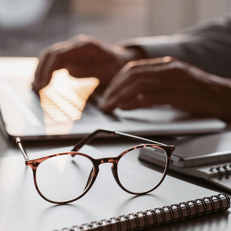 Glasögon i fokus framför någon som skriver på ett tangentbord.